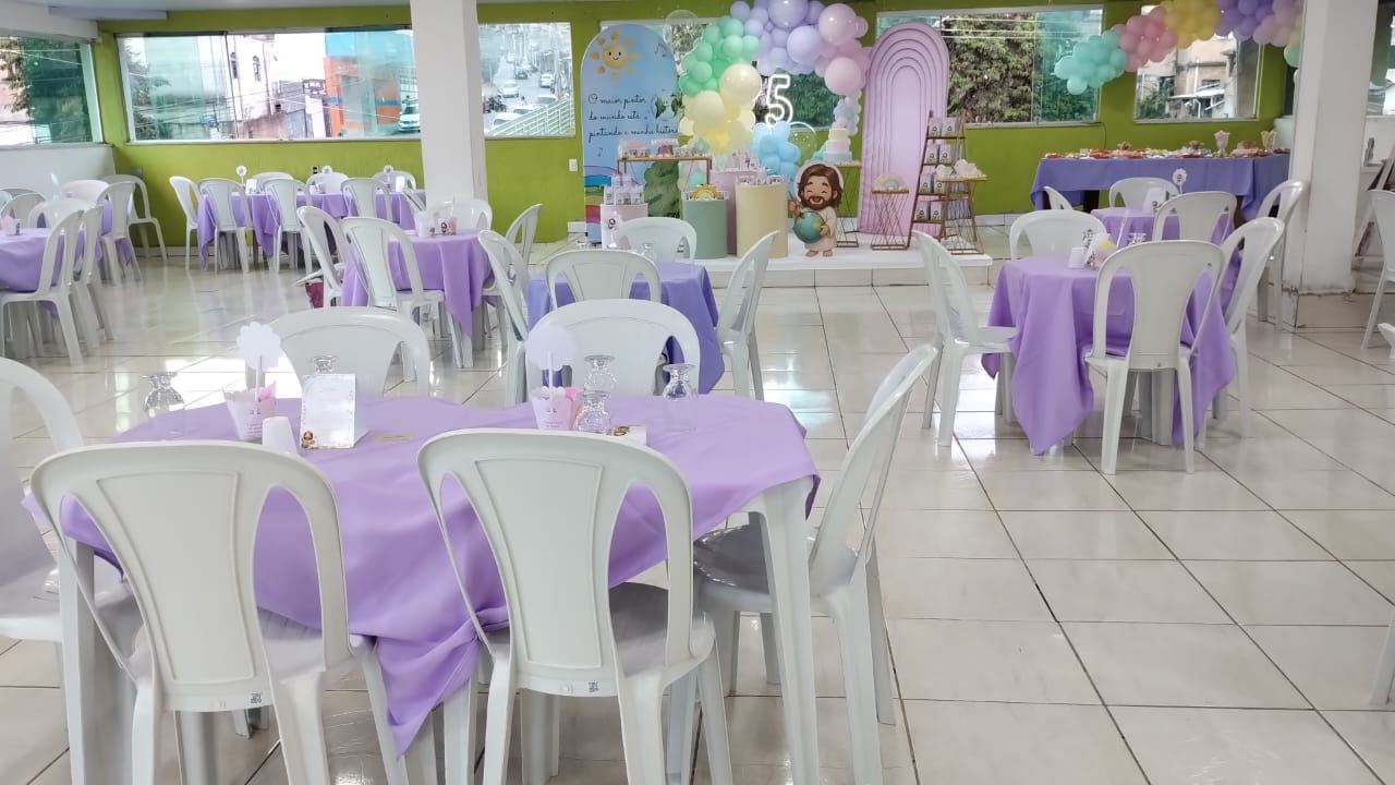 Salão de festa infantil com mesas de toalhas lilás e cadeiras brancas